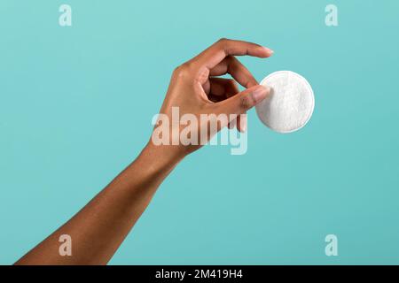 Blassschwarze Frau mit sauberem Wattepad zum Entfernen von Make-up vor türkisfarbenem Hintergrund Stockfoto