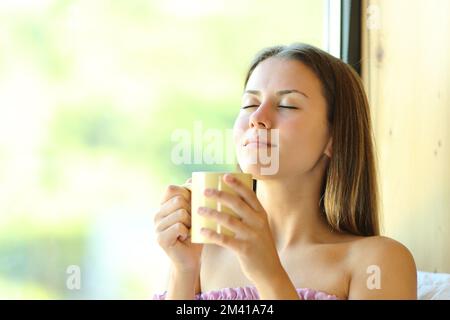 Entspannter Teenager, der Kaffee riecht, neben einem Fenster zu Hause Stockfoto