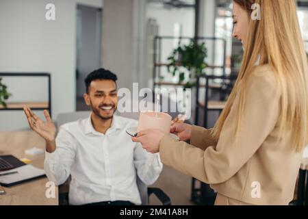 Ein junger Hindu-Mann ist dabei, Kerzen auf einem Kuchen auszublasen und sich während einer Geburtstagsfeier mit Kollegen etwas zu wünschen. Kollegen feiern eine Geburt Stockfoto