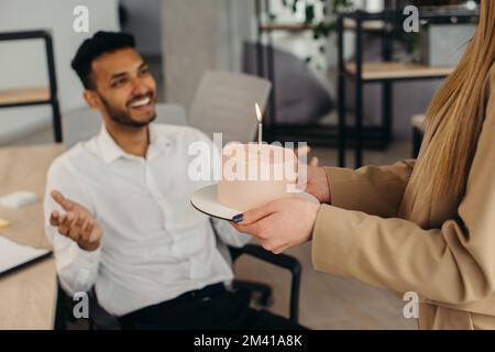 Ein junger Hindu-Mann ist dabei, Kerzen auf einem Kuchen auszublasen und sich während einer Geburtstagsfeier mit Kollegen etwas zu wünschen. Kollegen feiern eine Geburt Stockfoto