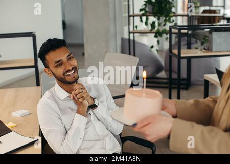 Ein junger Hindu-Mann ist dabei, Kerzen auf einem Kuchen auszublasen und sich während einer Geburtstagsfeier mit Kollegen etwas zu wünschen. Kollegen feiern eine Geburt Stockfoto