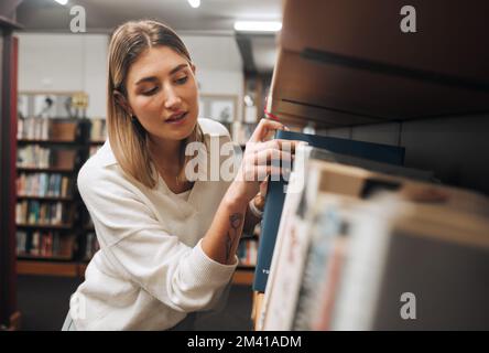 Mädchen-, Schüler- und Suchbücher in der Bibliothek für Bildung, Wissen und Lernen. Junge Frau, Universitätsstudentin und Bücherregal auf dem College Campus für Stockfoto