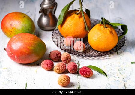 Ein Stillleben mit Lychees-Tangerinen und Mangos auf dem schäbigen Tisch Stockfoto