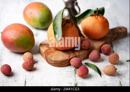 Ein Stillleben mit Lychees-Tangerinen und Mangos auf dem schäbigen Tisch Stockfoto