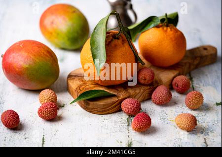 Ein Stillleben mit Lychees-Tangerinen und Mangos auf dem schäbigen Tisch Stockfoto