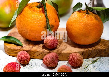 Ein Stillleben mit Lychees-Tangerinen und Mangos auf dem schäbigen Tisch Stockfoto