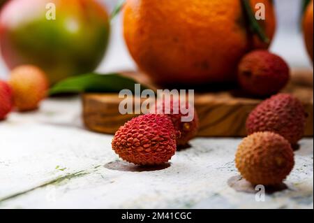 Ein Stillleben mit Lychees-Tangerinen und Mangos auf dem schäbigen Tisch Stockfoto