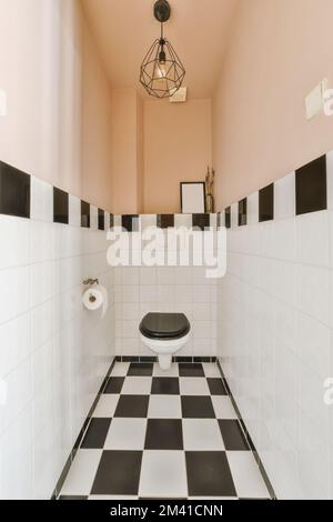 Ein Badezimmer mit rosafarbenen Wänden und schwarz-weißen Fliesen auf dem Boden, es gibt eine Toilette in der Ecke Stockfoto