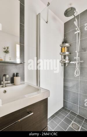 Ein modernes Badezimmer mit grauen Fliesen und weißen Armaturen im Duschkopf ist an der Wand über dem Waschbecken montiert Stockfoto