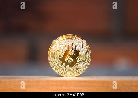 Goldene Bitmünze auf dem Holzschreibtisch mit ziegelrotem Hintergrund. Symbol für virtuelle Kryptowährung Stockfoto