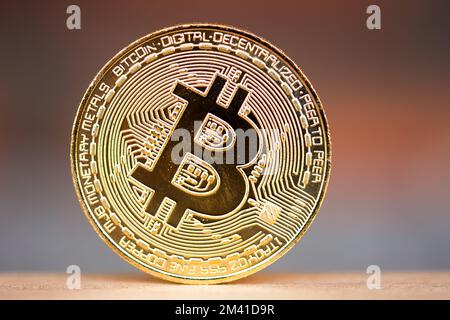 Goldene Bitmünze auf dem Holzschreibtisch mit ziegelrotem Hintergrund. Symbol für virtuelle Kryptowährung Stockfoto