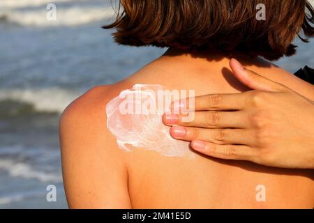 Die Hand streut liebevoll Sonnenschutzmittel auf den Rücken des kleinen Mädchens Stockfoto