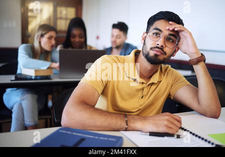 Indischer Mann, Student und gelangweilt im Klassenzimmer, müde und gestresst mit Notizen, Prüfungen oder Aufgaben. Junger Mann, männlich oder erschöpft für Ausbildung, Test oder Stockfoto