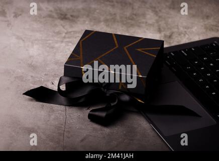 Schwarze Geschenkbox mit goldenen Streifen auf einer Laptop-Tastatur. Geschenke für Männer. Gut geeignet für Banner zum Vatertag oder zum Black Friday Online-Shopping. Stockfoto