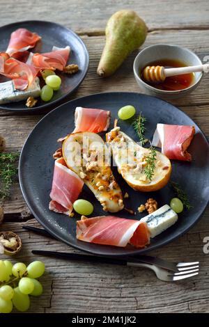 Gebackene Birnen gefüllt mit Gorgonzola-Käse, serviert mit Walnüssen und Südtiroler Speck Stockfoto