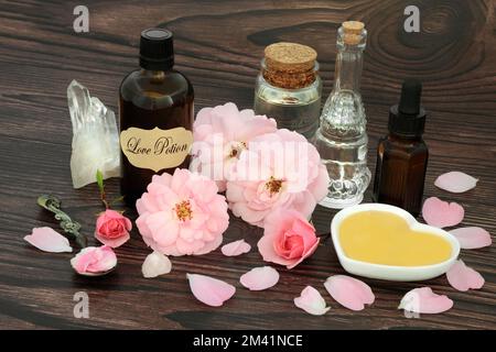 Valentinstag Liebestrank Zauberspruch Zutaten mit rosa Rosenblumen, Honig, Quarz Kristalle, Öl, Quellwasser. Stockfoto