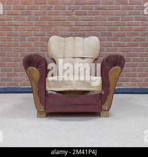 Ein alter Sessel mit Spuren der Zeit an einer Ziegelwand. Quadratisches Format Stockfoto
