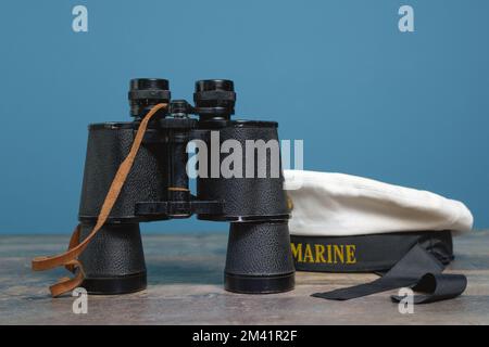 Versenden Sie Ferngläser und Kappe ohne Spitzen auf türkisfarbenem Hintergrund auf einem strukturierten Holztisch Stockfoto