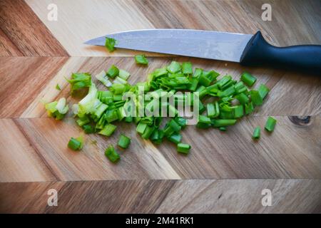 Schnittlauch der grünen Zwiebeln auf einem Schneidebrett schneiden. Dunkler Holzhintergrund. Draufsicht. Stockfoto