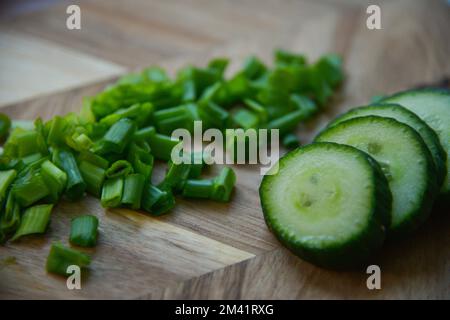Grüne frische Zwiebelscheiben mit grünen Gurkenscheiben auf einem Holzbrett Stockfoto