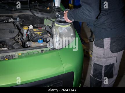 Alte Autoscheinwerfer polieren. Kfz-Servicetechniker mit Elektropolierer, der grüne Autohaube in der Kfz-Reparaturwerkstatt poliert Stockfoto