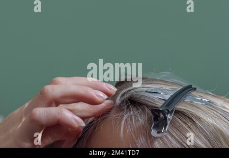 Position der Fixierung der Haare am Kopf während des Färbevorgangs. Schließen. Grüner Hintergrund Stockfoto