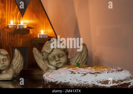 Festliches Weihnachtsgeschenk bestehend aus Kerzen, Engelsstatuen und einem Kuchen auf einem Tisch. Stockfoto