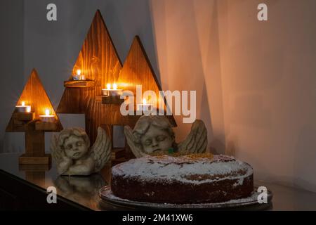 Festliches Weihnachtsgeschenk bestehend aus Kerzen, Engelsstatuen und einem Kuchen auf einem Tisch. Stockfoto