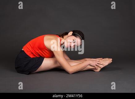 Weibliche Gymnast in einem roten Hemd und schwarzen Hosen dehnen und Aufwärmen - Teil einer Serie Stockfoto