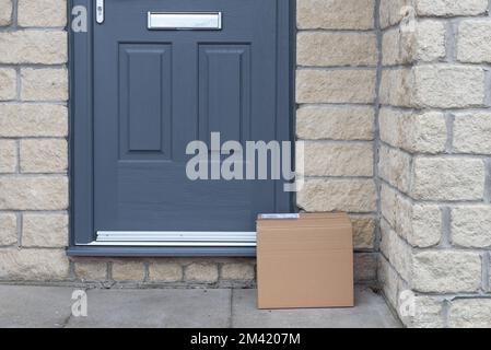 Kleines Papppäckchen, das auf der Treppe liegt. Graue Tür und Tür. Kurierdienst-Zustellpaket. Stockfoto