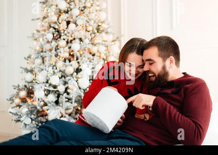 Glückliches Paar in der Nähe von Geschenkschachteln und weihnachtsbaum. Ein Paar umarmt sich und schaut sich an, nahe dem weihnachtsbaum. Stockfoto