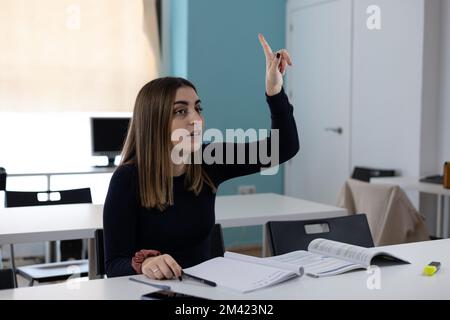 Junge Studentin, die Hand hebt und während des Unterrichts an den Professor fragt Stockfoto