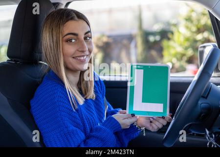 Fröhliche junge Fahrerin zeigt ihr L-Schild lerner spain Autoescuela Stockfoto