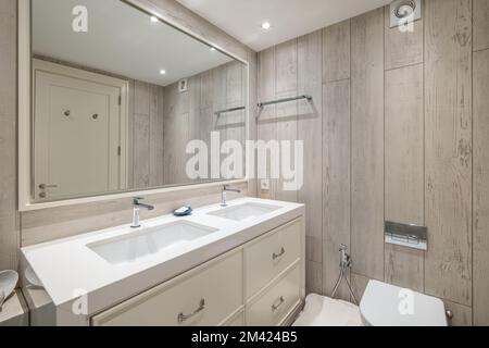 Wunderschönes Bad in beruhigenden Pastelltönen mit großem Spiegel, der von Tür zu Badewanne reflektiert. Der Raum ist hell und mit Lampen in glänzendem Stretch ausgestattet Stockfoto