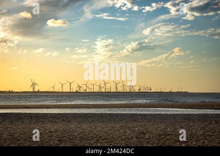 Sonnenuntergang an einem tropischen Strand. In der Ferne eine Farm mit erneuerbaren Energien. Freier Speicherplatz zum Schreiben. Stockfoto