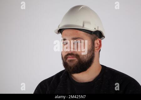 Porträt eines Mannes mit weißem Schutzhelm auf weißem isoliertem Hintergrund. Stockfoto