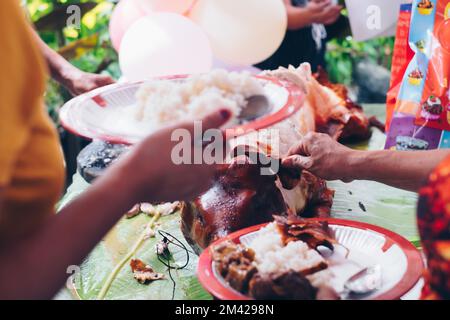 Metzger, der in Stücke schneidet, der allzeit beliebte Favorit, das beliebte köstliche, gebratene, knusprige ganze Schweinefleisch oder Lechon Baboy, lag auf Bananenblatt auf dem Tisch Stockfoto