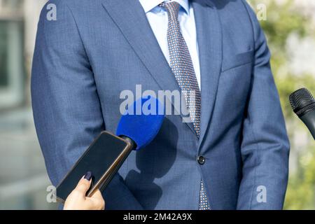 Reporter auf der Pressekonferenz hält Mikrofon und Smartphone und macht Medieninterviews Stockfoto