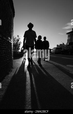 Lange Schatten von einer Familie, die von der untergehenden Sonne beleuchtet wird Stockfoto