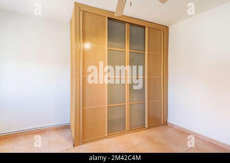Ein maßgeschneiderter Kleiderschrank aus Holz mit Schiebetüren aus Holz und Glas in einem leeren Raum Stockfoto