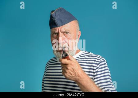 Ein alter Seemann mit einer Rauchpfeife. Porträt eines Seemanns in einem gestreiften Hemd und einer blauen Mütze Stockfoto