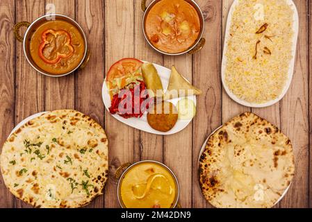 Stille indische Gerichte mit Hühnchen- und Lamm-Curry, Basmati-Reis, Käse-Naan, gelbes Curry, Vorspeisenteller mit gebratenen Zwiebeln und Samosa Stockfoto