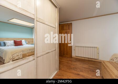 Schlafzimmer mit einem Doppelbett, Kleiderschrank mit weißen Schiebetüren und Spiegeln und dunklem Holzfußboden Stockfoto