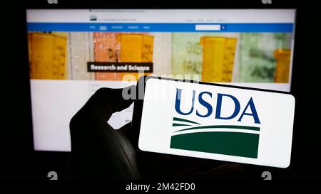 Person, die ein Mobiltelefon mit dem Logo des US-Landwirtschaftsministeriums (USDA) auf dem Bildschirm vor der Webseite hält. Konzentrieren Sie sich auf das Display des Telefons. Stockfoto