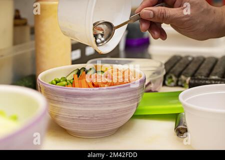 Ein Koch, der in einer asiatischen Küche eine Lachs-Schüssel mit Mohnsamen zubereitet Stockfoto