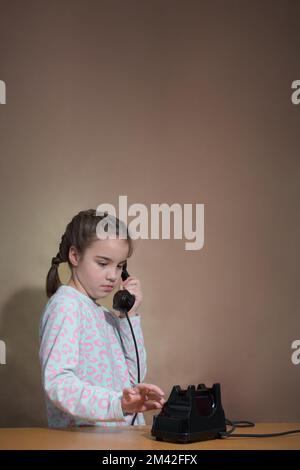 Retro-Porträt eines traurigen Mädchens. Vertikal. Speicherplatz kopieren. Das Teenager-Mädchen wählt eine Nummer auf einem alten Telefon. Stockfoto