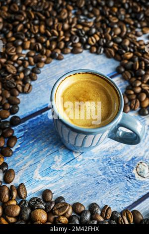 Eine hübsche blaue Tasse frisch gebrühten Espresso mit Schaum, umgeben von duftenden gerösteten Bohnen Stockfoto
