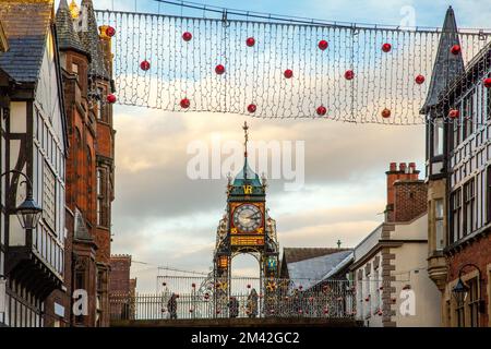 Blick auf die viktorianische Eastgate-Uhr und den Uhrenturm, der an den römischen Stadtmauern in der Eastgate Street Chester während der Weihnachtslichter von 2022 steht Stockfoto