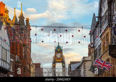 Blick auf die viktorianische Eastgate-Uhr und den Uhrenturm, der an den römischen Stadtmauern in der Eastgate Street Chester während der Weihnachtslichter von 2022 steht Stockfoto