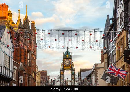 Blick auf die viktorianische Eastgate-Uhr und den Uhrenturm, der an den römischen Stadtmauern in der Eastgate Street Chester während der Weihnachtslichter von 2022 steht Stockfoto